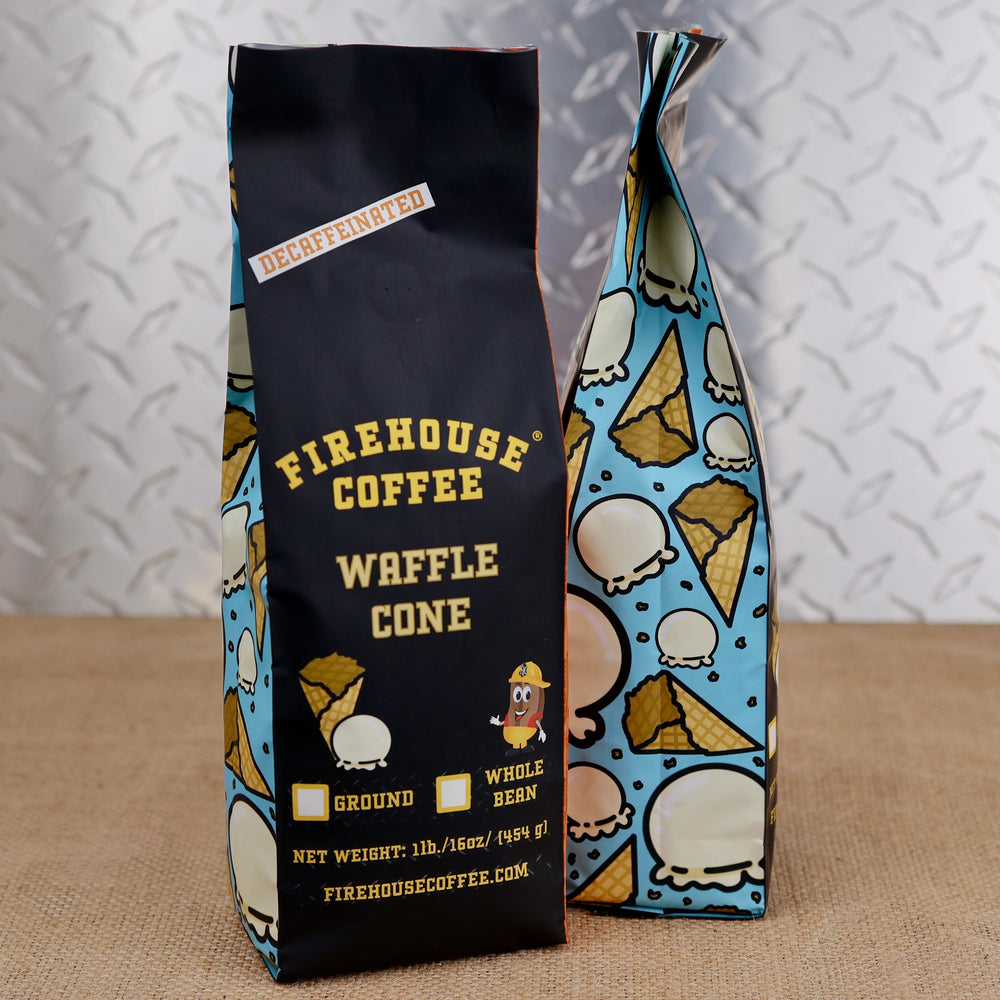 Two bags of Firehouse Coffee Waffle Cone decaffeinated ground and whole bean coffee, one standing upright with a black and blue patterned design and the other leaning against it, set on a burlap surface against a diamond plate metal background.