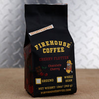 Firehouse Coffee Decaffeinated Cherry Flutter Chocolate Cherry flavored coffee in a 12 oz bag featuring rich chocolate and ripe cherry flavor notes. Swiss Water Process decaf coffee available in ground or whole bean, packaged in Firehouse Coffee's signature black bag with chocolate and cherry artwork and firefighter bean mascot.