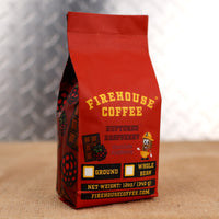 Red Firehouse Coffee bag with yellow text on a textured surface with raspberries and chocolate bars on the side.  