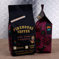 Two bags of Firehouse Coffee Irish Cream & Raspberry flavored whole bean coffee, one standing upright in black packaging and the other leaning behind it in dark raspberry-colored packaging, set on a burlap surface against a metallic diamond plate background.