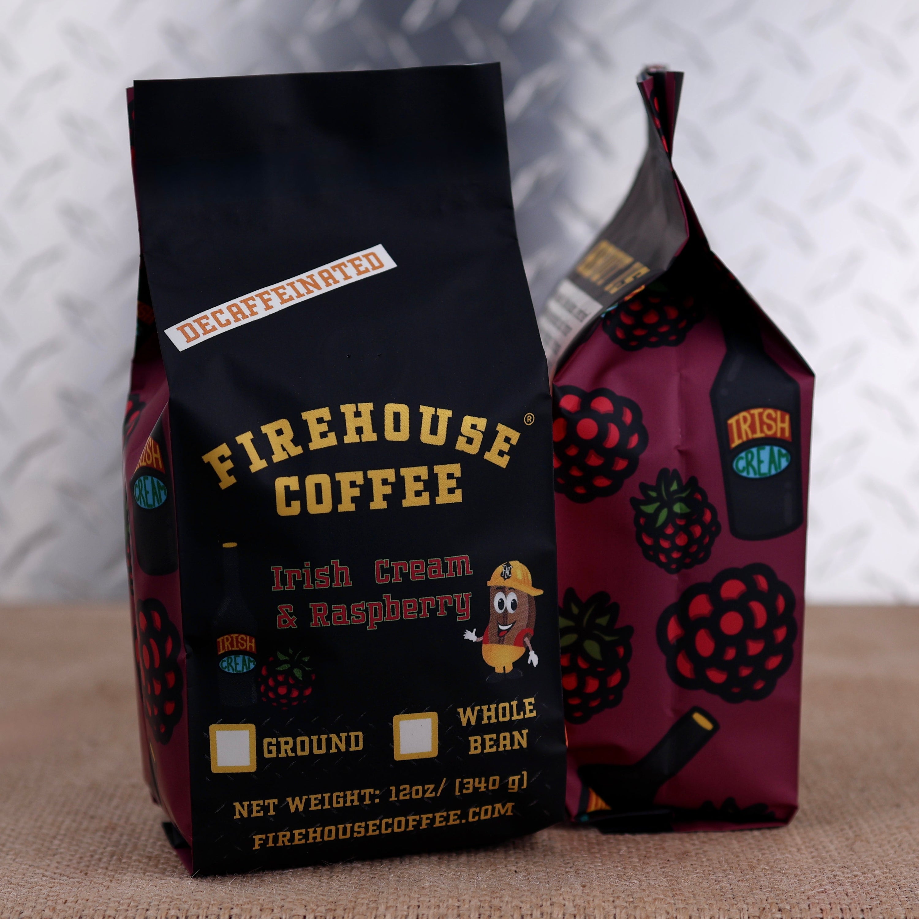 Two bags of Firehouse Coffee Irish Cream & Raspberry flavored whole bean coffee, one standing upright in black packaging and the other leaning behind it in dark raspberry-colored packaging, set on a burlap surface against a metallic diamond plate background.