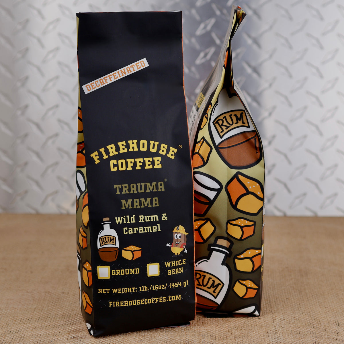 Two 1lb bags of Firehouse Coffee Trauma Mama Wild Rum & Caramel coffee standing on a burlap surface against a diamond plate metal background. One bag is solid black with yellow text, and the other features a cream, brown, and orange illustrated design with coffee beans and rum bottle graphics.