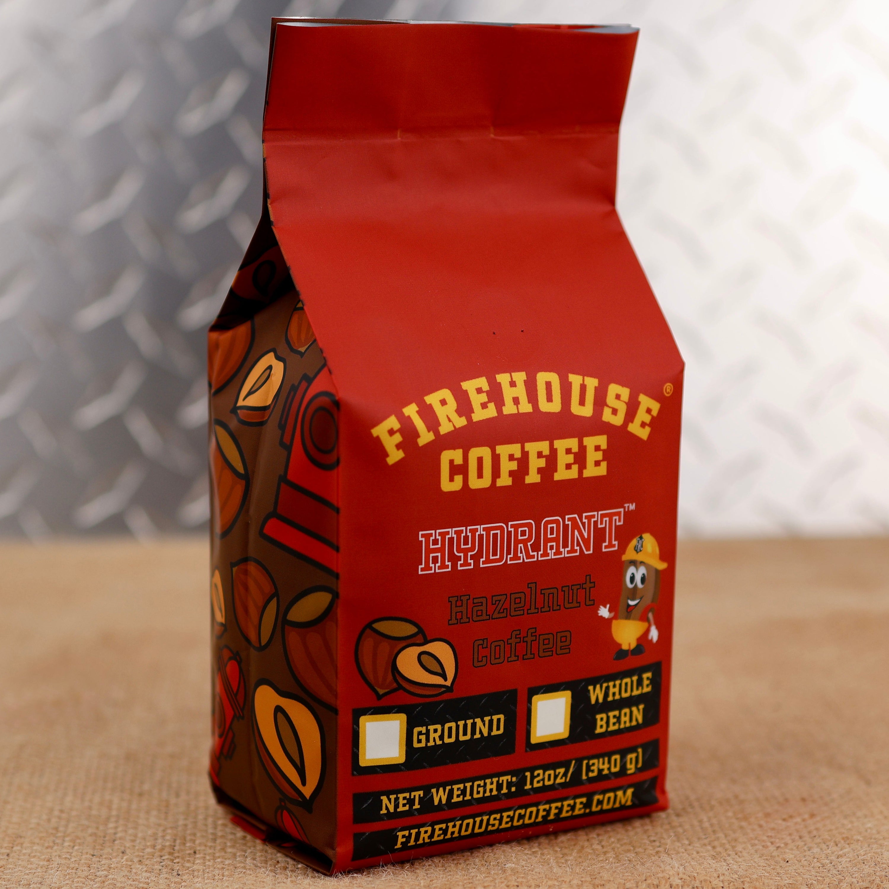 Firehouse Coffee Hydrant Hazelnut Coffee in a 12 oz red coffee bag featuring roasted hazelnut flavor, Firehouse Coffee branding, hazelnut graphics, and options for ground or whole bean coffee.