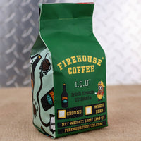 A green 12-ounce bag of Firehouse Coffee Irish Cream Coffee is displayed on a burlap-covered surface with a soft gray patterned background. The front label features the Firehouse Coffee logo, the product name I.C.U. Irish Cream Ultimate, an Irish cream bottle graphic, and the Firehouse coffee bean mascot wearing a firefighter helmet. The package includes checkboxes for ground or whole bean coffee, displays the net weight of 12 ounces (340 grams), and lists FirehouseCoffee.com at the bottom of the label.